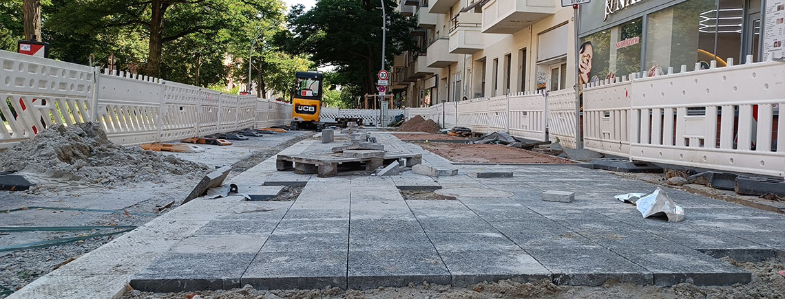 Das Foto zeigt die neue aber noch unfertige Bushaltestelle. Gerade werden Gehwegplatten verlegt.